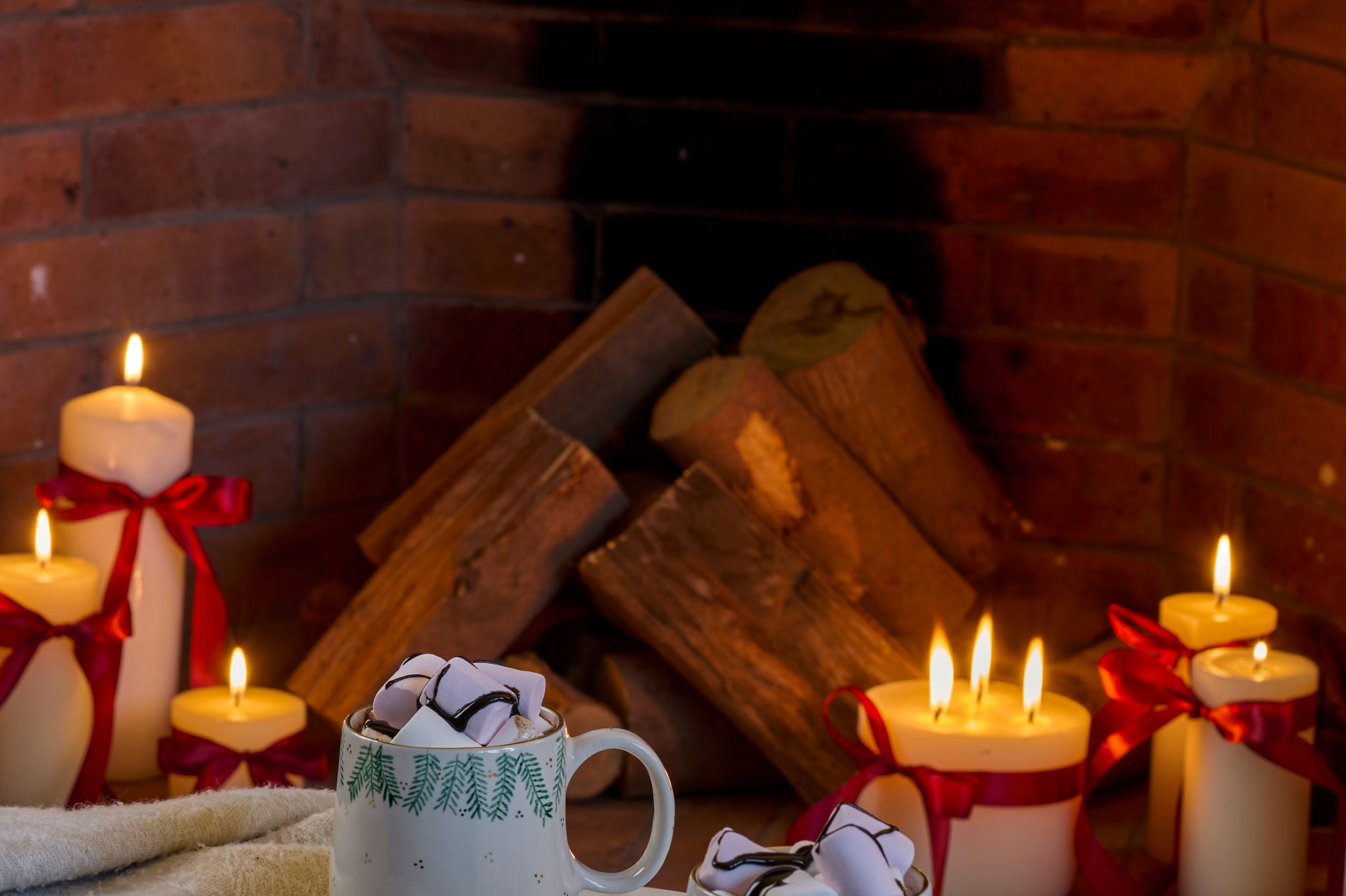 Two mugs with whipped cream and cookies on a marble surface in front of a fireplace with candles.